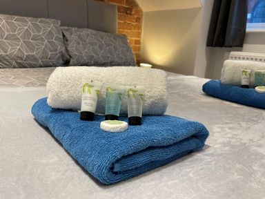 A bedroom with gray patterned bedding blue and white towels with small shampoo conditioner and shower gel bottles on the bed at Pams House in Weymouth