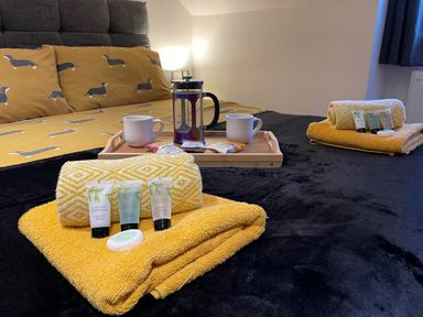 A bedroom with a bed covered in black and mustard dog patterned bedding with folded yellow towels and toiletries on the bed at Pams House in Weymouth