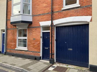 A street view of a brick house with a blue door and garage door at Pams House in Weymouth