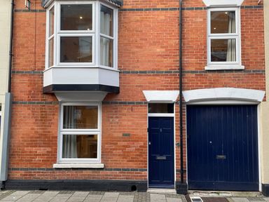 A brick house with white framed windows a blue door and blue garage door at Pams House in Weymouth