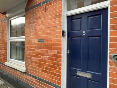 A blue front door with the number 5 on a red brick house with a white window and a sign that reads Pams House in Weymouth