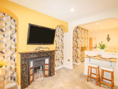 A living room with a fireplace a wall mounted television and a breakfast bar with stools at Pams House in Weymouth