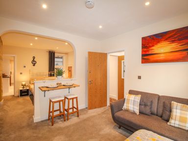 A living room with a grey sofa and bar stools with plates next to an open doorway at Pams House in Weymouth