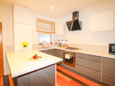 A kitchen with grey cabinets white countertops a window with blinds and a built in oven at Pams House Weymouth
