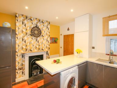 A kitchen with a washing machine under the counter next to a sink and a fireplace with geometric wallpaper at Pams House in Weymouth