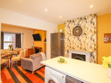 An open-plan kitchen and dining area with a patterned fireplace wall and a dining table with chairs at Pam's House in Weymouth