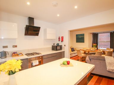 A kitchen with a stove oven microwave and yellow flowers on the counter opening to a dining area with a table chairs and sofa at Pams House in Weymouth