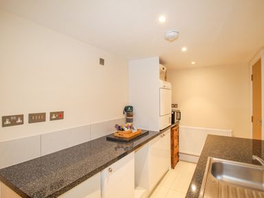 A kitchen with black countertops white cabinets a microwave a white appliance and a stainless steel sink at Pams House in Weymouth