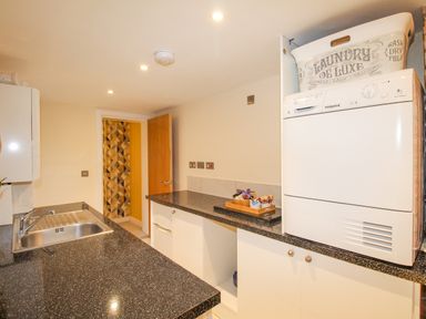 A utility room with a washing machine dryer a sink countertop cabinets and an open door leading to another room at Pams House in Weymouth