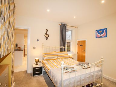 A bedroom with a metal bed frame a nightstand with a lamp geometric patterned wallpaper and a door at Pams House in Weymouth