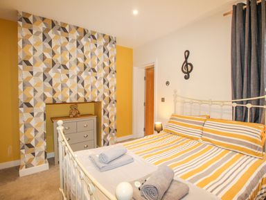 A bedroom with a bed striped yellow and gray bedspread a chest of drawers a teddy bear and geometric patterned wallpaper at Pams House in Weymouth