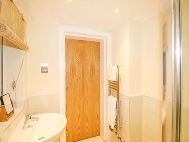 A bathroom with a wooden door a sink mirror a towel rack with towels and a window blind at Pams House in Weymouth