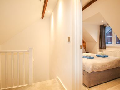 A hallway with carpeted stairs and a bedroom with a bed and window at Pams House in Weymouth