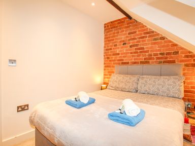 A bedroom with a double bed towels on bed against a brick wall at Pams House in Weymouth