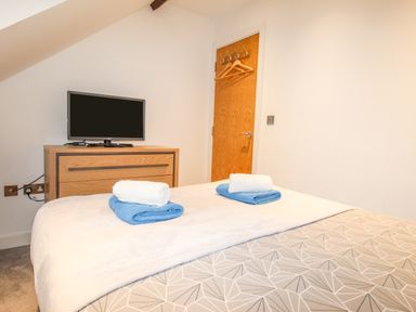 A bedroom with a bed towels folded on the bed a wooden chest of drawers with a television and a door with hangers at Pams House in Weymouth