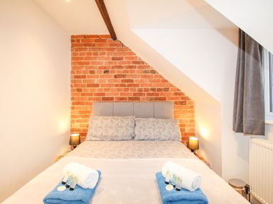 A bedroom with a double bed against a brick wall under a slanted ceiling with bedside lamps at Pam's House in Weymouth