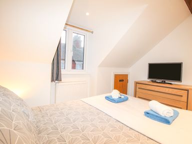 A bedroom with a patterned bedspread towels on the bed a wooden dresser with a TV and a window at Pams House in Weymouth