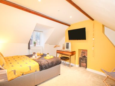 A bedroom with a bed and yellow bedding a television mounted on a yellow wall and a small vanity at Pams House in Weymouth