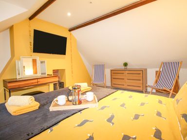 A bedroom with a yellow wall mounted tv a wooden dresser two striped deck chairs and a bed with a duck patterned duvet at Pams House in Weymouth