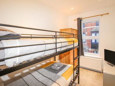 A bedroom with a bunk bed and wooden wardrobe next to a window with dark curtains at Pams House in Weymouth