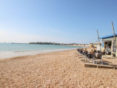 A pebble beach with outdoor cafe tables and chairs near the water at Pam's House in Weymouth