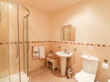 A bathroom with a glass shower enclosure a pedestal sink a toilet a small cabinet and towels hanging on a wall at Ptarmigan Lodge in Glengoulandie near Aberfeldy