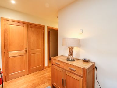 A hallway with wooden double doors a wooden cabinet with a lamp and a small bowl on it at Ptarmigan Lodge in Glengoulandie near Aberfeldy