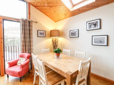 A dining room with a wooden table and white chairs by a window with a red armchair and framed pictures on the wall at Ptarmigan Lodge in Glengoulandie near Aberfeldy