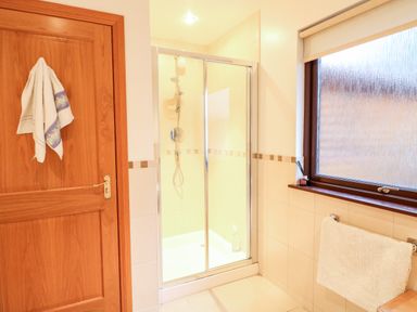 A bathroom with a shower enclosure a wooden door with a towel a window and a towel rack at Ptarmigan Lodge in Glengoulandie near Aberfeldy