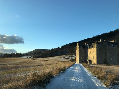 A stone castle next to a snow-covered path with fields and hills in the background at Ptarmigan Lodge in Glengoulandie near Aberfeldy