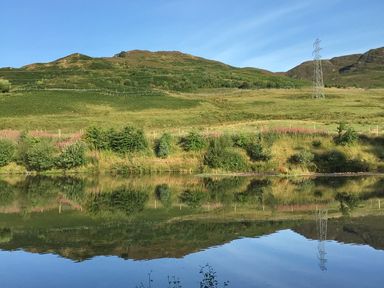 A landscape with hills trees and a body of water reflecting the scenery at Ptarmigan Lodge in Glengoulandie near Aberfeldy
