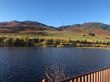 A lake with hills and vegetation in the background at Ptarmigan Lodge in Glengoulandie near Aberfeldy