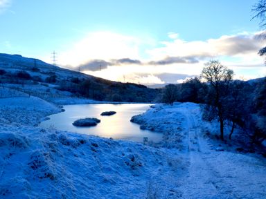 A snowy landscape with a partially frozen river hills trees and power lines at Ptarmigan Lodge in Glengoulandie near Aberfeldy