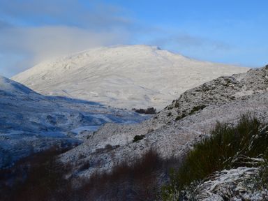 A snowy mountain landscape with hills and sparse vegetation under a partly cloudy blue sky