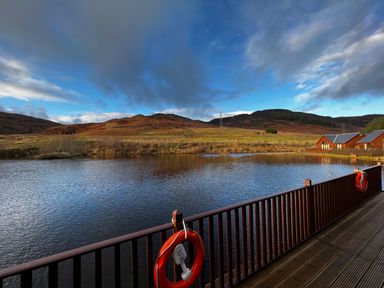 A lake with wooden deck and railings with lifebuoys and hills in the background at Ptarmigan Lodge in Glengoulandie near Aberfeldy