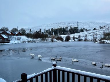 A frozen lake with swans and snow-covered houses and hills in the background at Ptarmigan Lodge in Glengoulandie near Aberfeldy