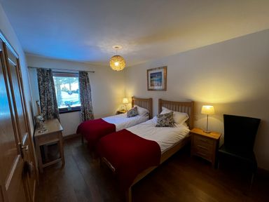 A bedroom with two single beds with red blankets and a desk near the window at Ptarmigan Lodge in Glengoulandie near Aberfeldy