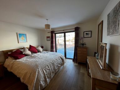 A bedroom with a large bed with pillows next to sliding glass doors overlooking snow outside at Ptarmigan Lodge in Glengoulandie near Aberfeldy