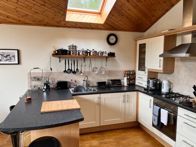 A kitchen with black countertop, white cabinets, stove, sink, hanging utensils, and wooden ceiling at Ptarmigan Lodge in Glengoulandie near Aberfeldy