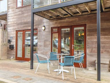 A wooden patio with a round table and four chairs outside double glass doors at Tolcarne in Porthtowan