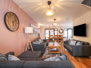 A living room with gray sofas a wooden coffee table wall clock and dining table at Tolcarne in Porthtowan