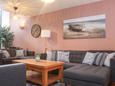 A living room with dark gray sofas patterned cushions wooden coffee table clock plant and a painting of a boat at Tolcarne in Porthtowan