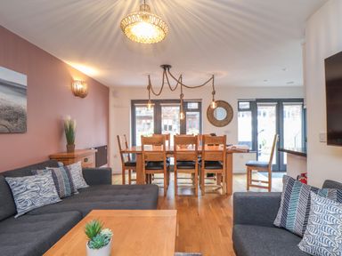 A living and dining area with sofas pillows dining table chairs and decorative lighting at Tolcarne in Porthtowan