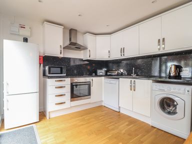 A kitchen with white cabinets black countertops a refrigerator microwave oven dishwasher and washing machine at Tolcarne in Porthtowan