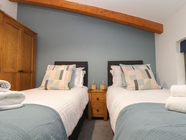 A bedroom with two single beds a wooden wardrobe and a wooden nightstand at Tolcarne in Porthtowan