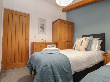A bedroom with two single beds wooden wardrobe and chest of drawers at Tolcarne in Porthtowan