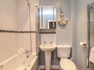 A bathroom with a bathtub shower sink toilet wall mirror and towel rail at Tolcarne in Porthtowan