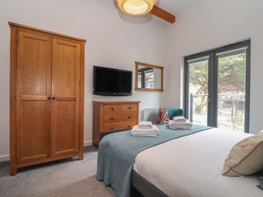 A bedroom with a bed and folded towels a wooden wardrobe a wooden dresser a wall-mounted TV a chair and double glass doors at Tolcarne in Porthtowan