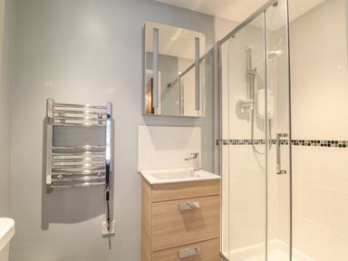 A bathroom with a wooden vanity unit with sink a mirror a glass shower enclosure and a chrome towel radiator at Tolcarne in Porthtowan