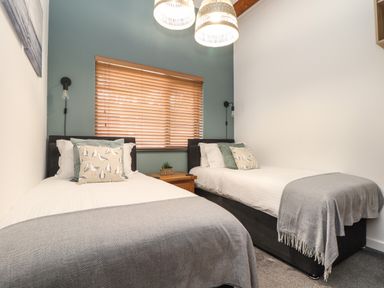 A bedroom with two single beds a wooden side table and window blinds at Tolcarne in Porthtowan